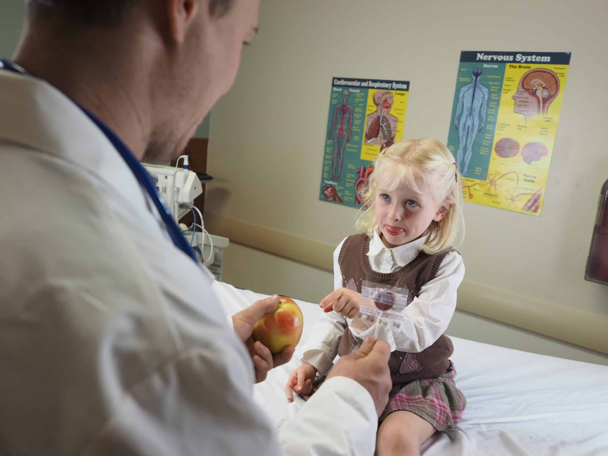Doctor giving an apple to a little girl in a hospital under the lights