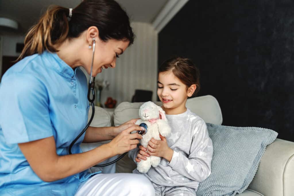 Smiling girl sitting on sofa and holding her bunny toy. Doctor trying to relax girl so she is pretending to examining her bunny with stethoscope.